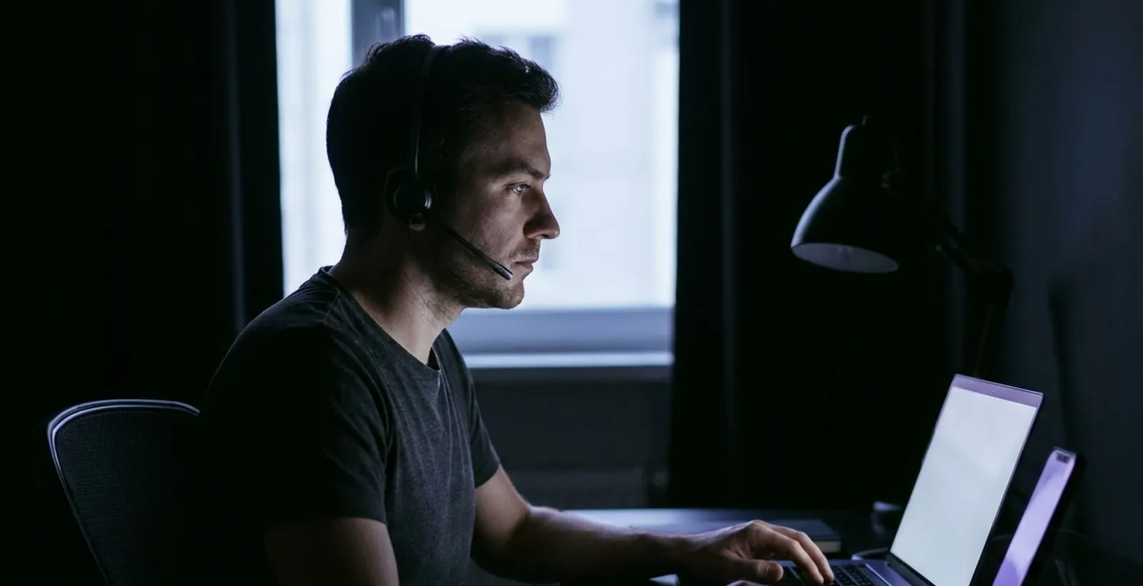 A remote agent at a tidy desk lit by a laptop screen